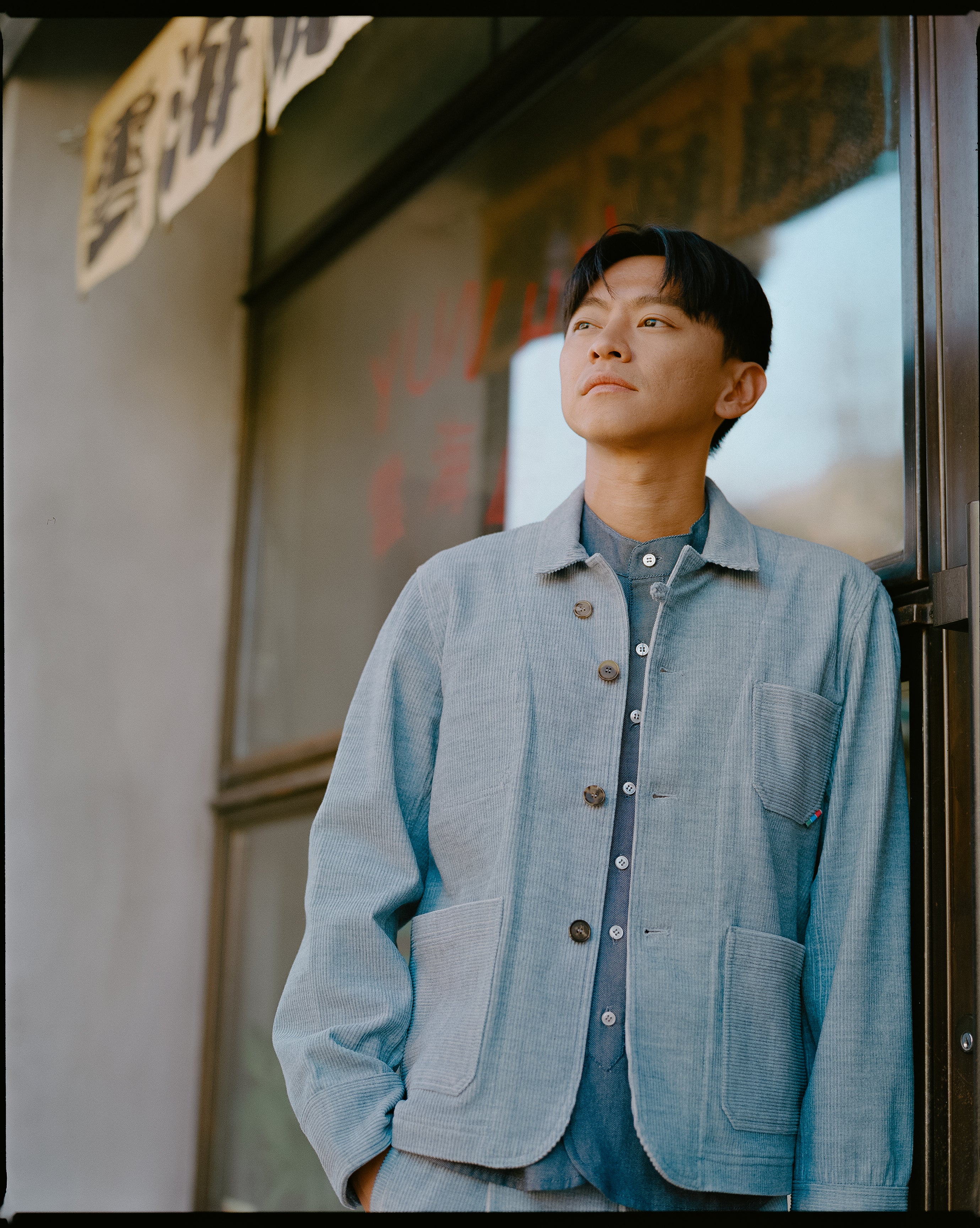 Man wearing a light blue corduroy jacket standing in front of a store with glass doors.