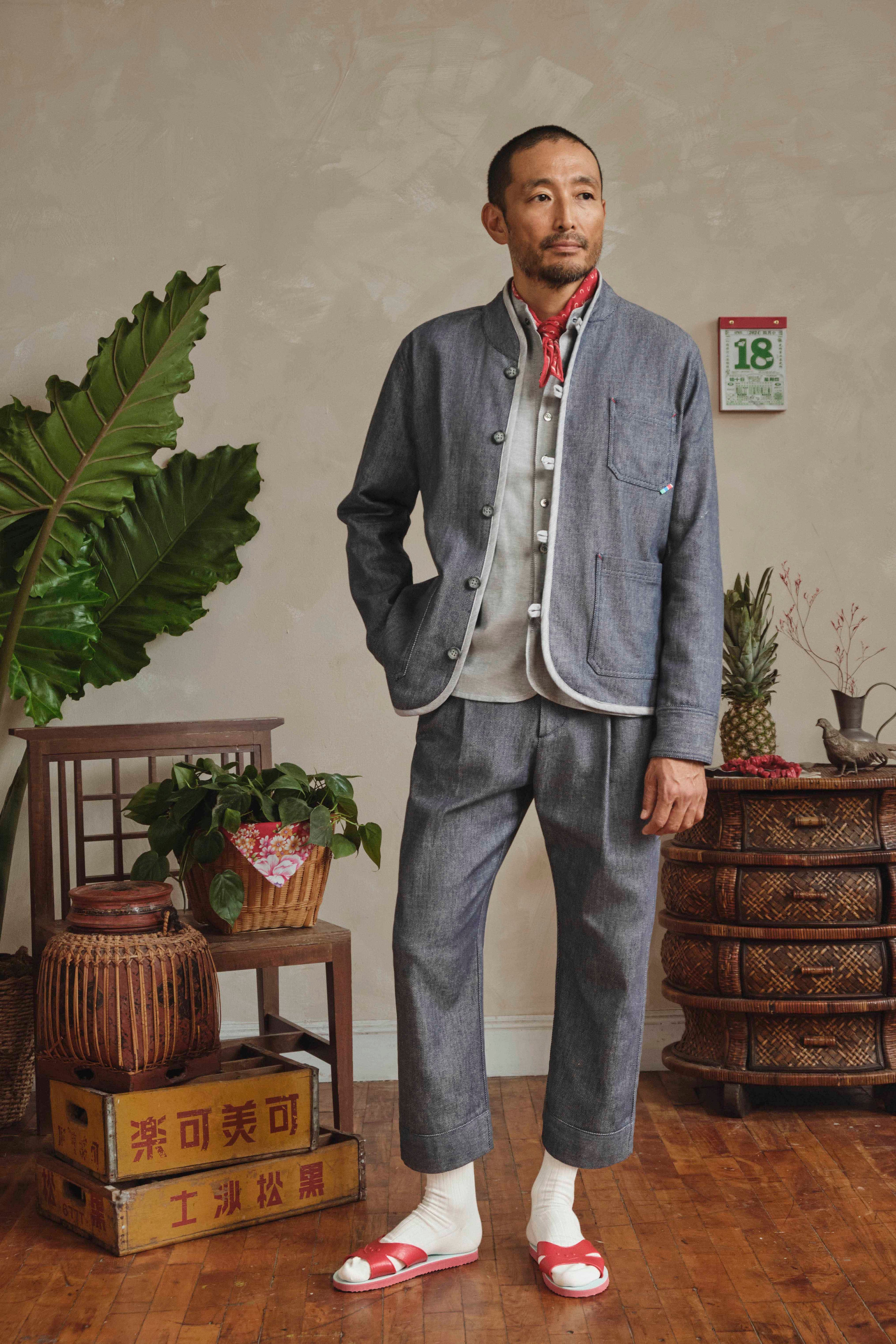 Man in a denim Tang suit standing in a room with plants and furniture.