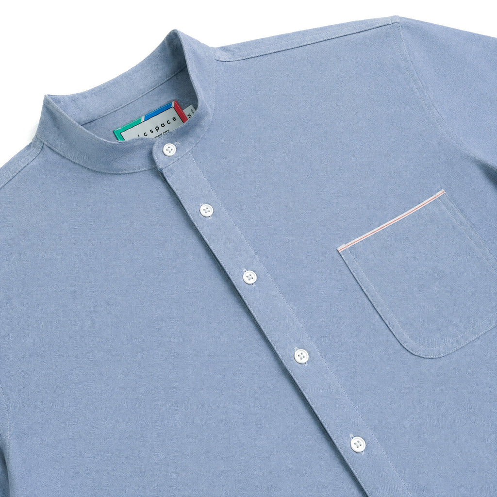 A close-up of a light blue long-sleeve button-up shirt with a mandarin collar, white buttons, and a chest pocket accented with thin red and white stripes.