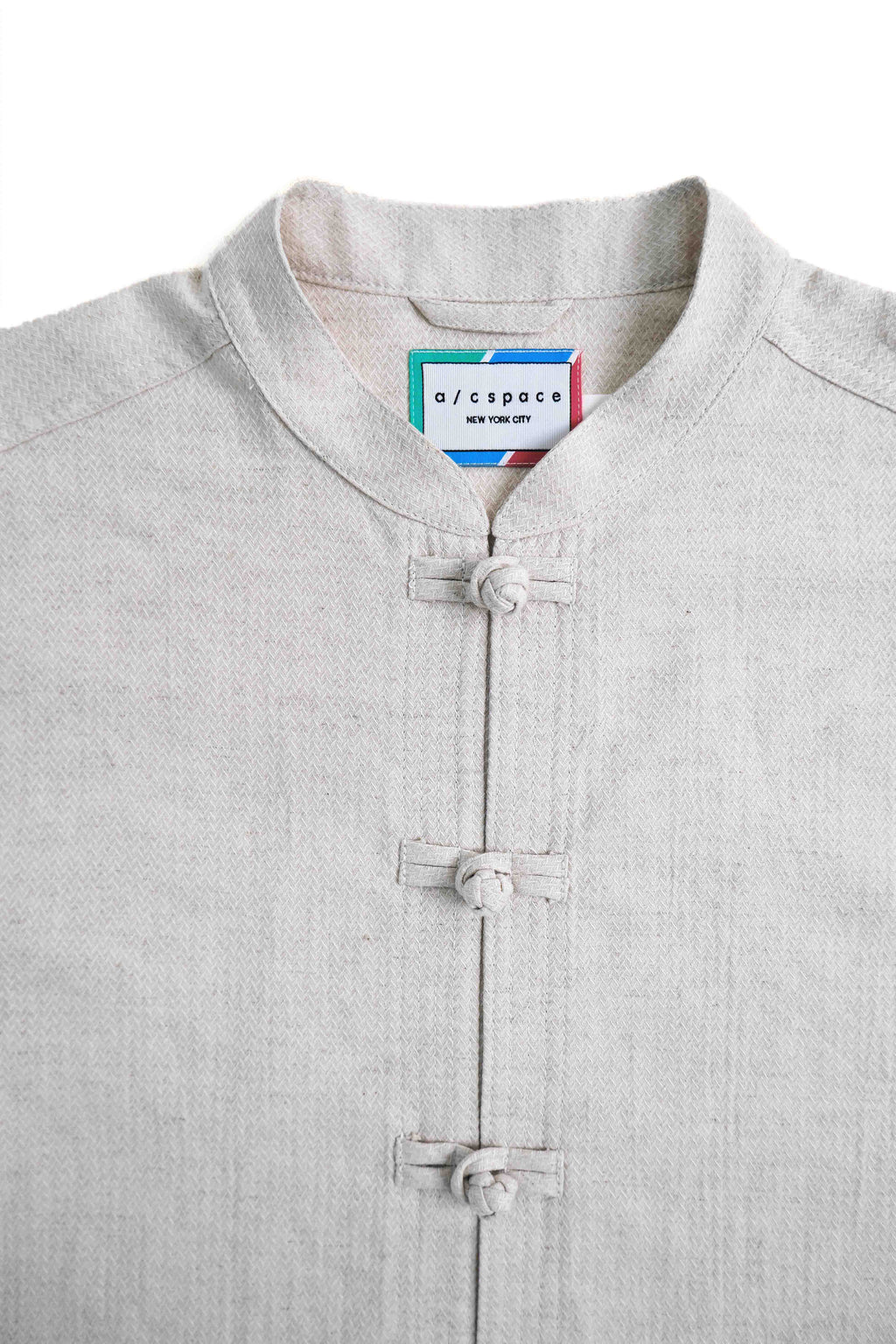 A close-up of a light gray linen mandarin collar shirt with traditional Chinese-style frog closures, featuring a visible 'o/cropco' neck label.