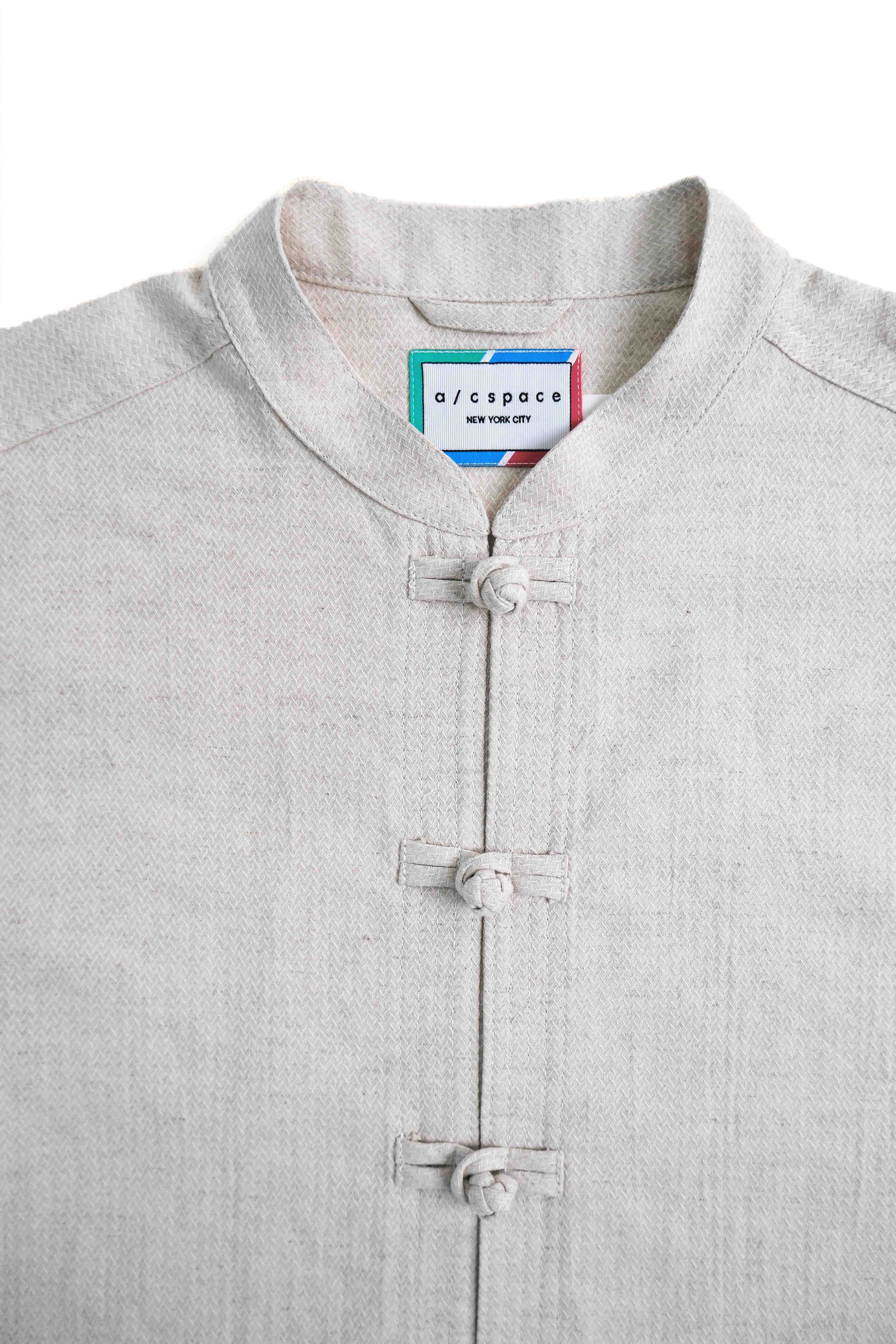 A close-up of a light gray linen mandarin collar shirt with traditional Chinese-style frog closures, featuring a visible 'o/cropco' neck label.