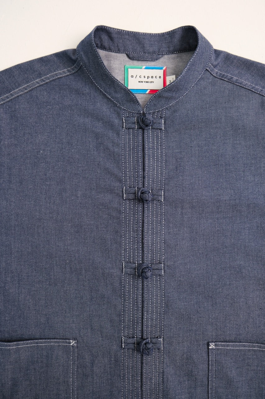 A close-up of a dark indigo chambray jacket with a mandarin collar and traditional Chinese-style button closures.