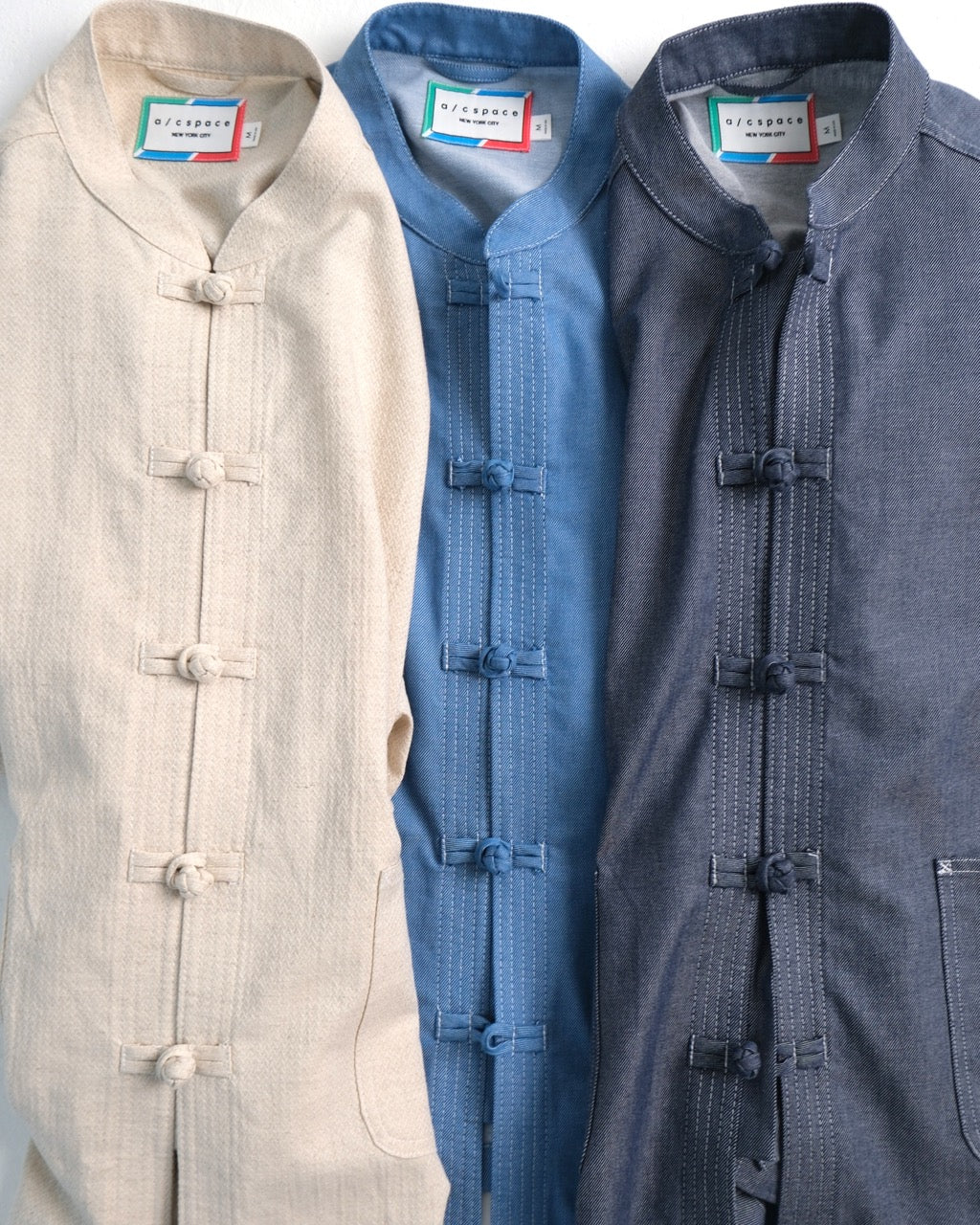 Three traditional Chinese-style jackets in beige, blue, and navy, featuring mandarin collars and decorative button closures, displayed side-by-side.